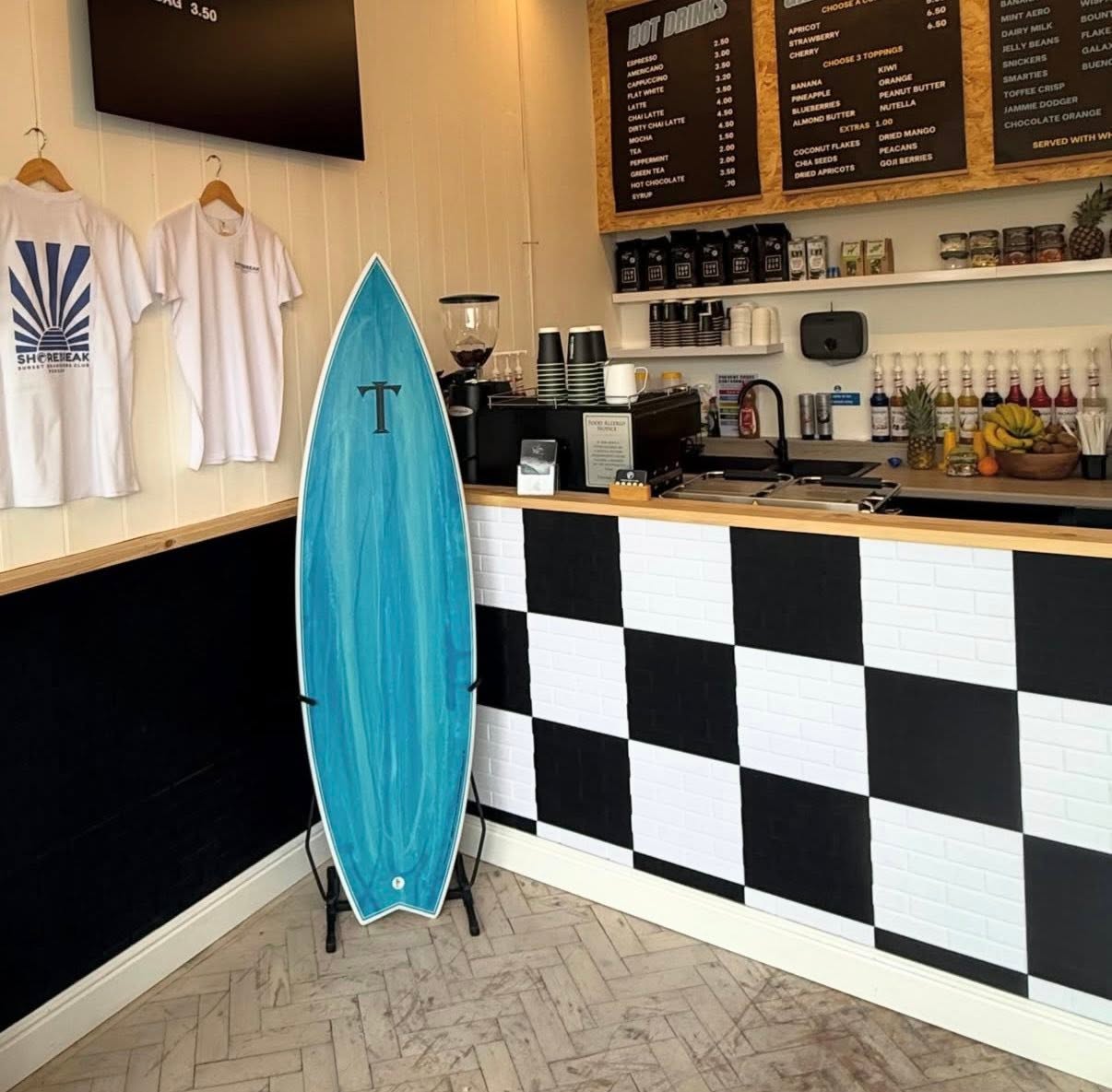 Inside Shorebreak, surfboard and merchandise beside the checkerboard counter